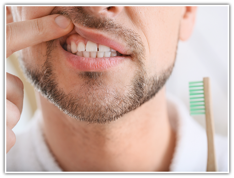 Man holding toothbrush and pulling up lip to show gums