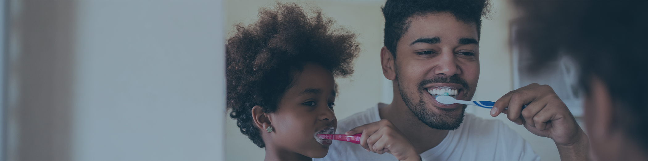 Parent and child brushing teeth in bathroom mirror