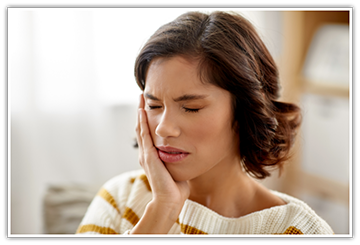 Woman in striped sweater rubbing her jaw in pain