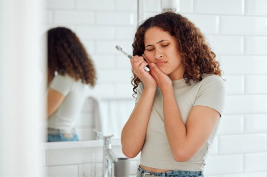 Woman holding a toothbrush and rubbing her aching jaw