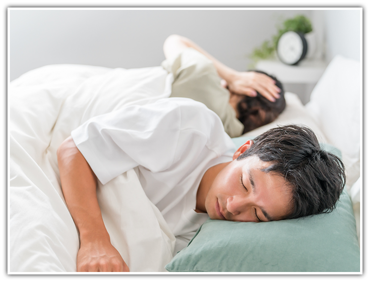 Man sleeping in bed while woman covers ears in background