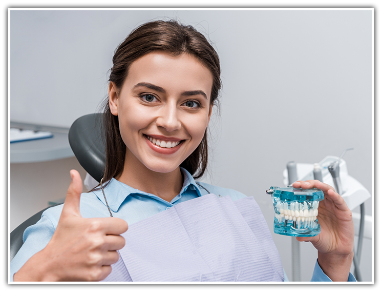 Woman in dental chair giving thumbs up while holding a model of teeth