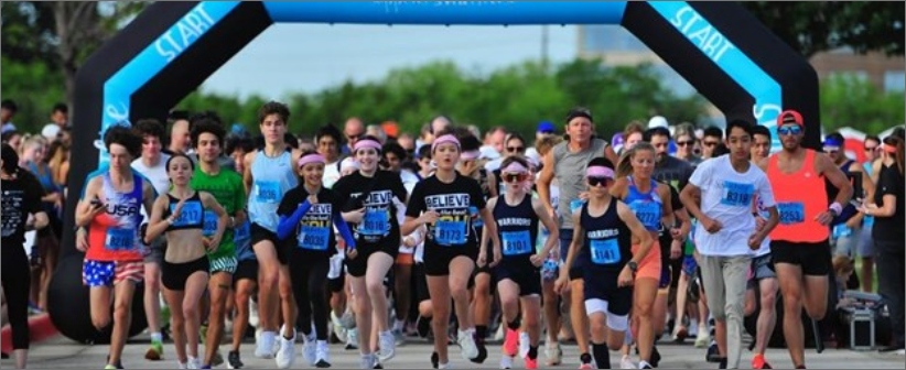 A diverse group of runners enthusiastically starts a race, passing under a blue inflatable arch that reads Run4Elise.